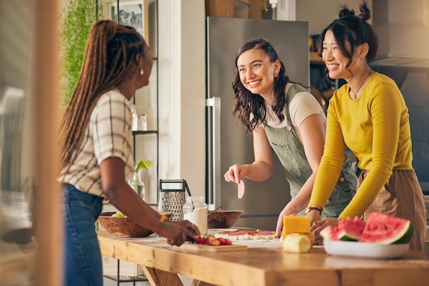 Amigos sonríen y mujeres cocinando pizza en la cocina uniéndose y divirtiéndose juntas en casa Chicas felices horneando comida margherita y pan de salami en el almuerzo queso con carne y brunch en casa