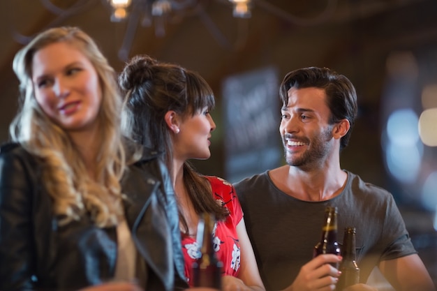 Amigos sonrientes mirándose mientras sostienen botellas de cerveza