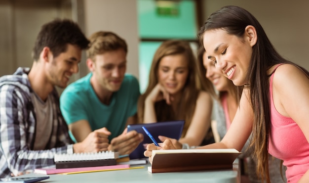 Amigos sonrientes que se sientan estudiando y que usan la PC de la tableta