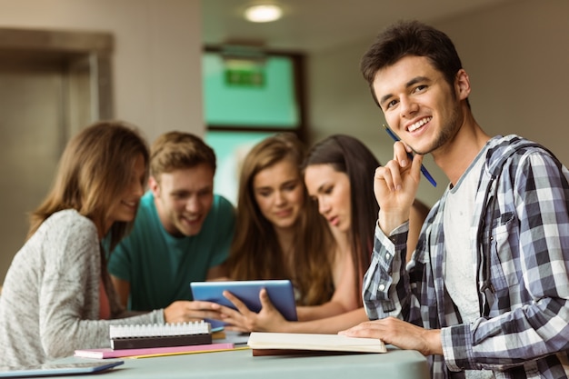 Amigos sonrientes que se sientan estudiando y que usan la PC de la tableta