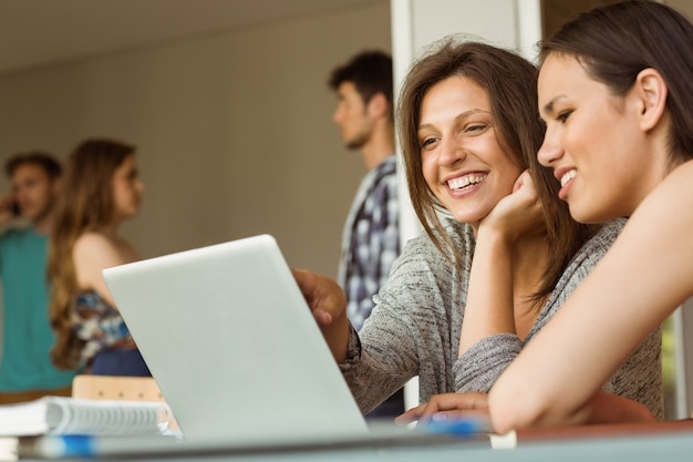 Foto amigos sonrientes que se sientan usando la computadora portátil