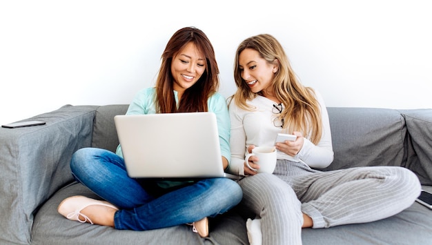 Amigos sonrientes sentados con teléfonos móviles y portátiles en el sofá de casa