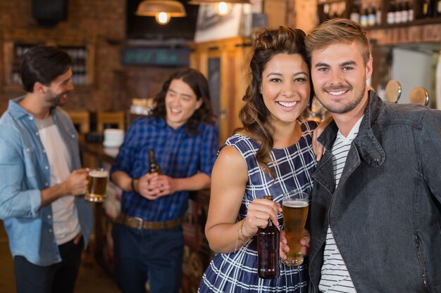 Amigos sonrientes sosteniendo un vaso y una botella de cerveza en el pub