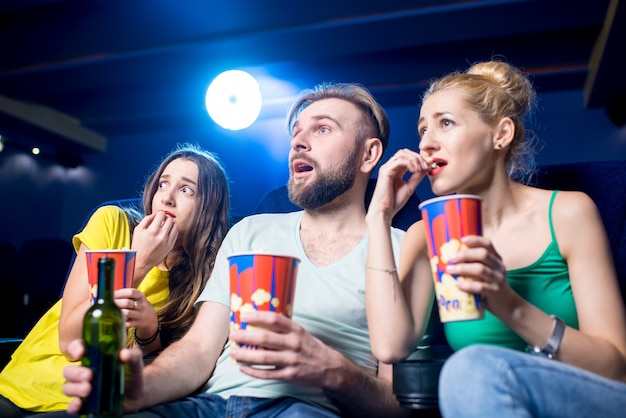 Amigos sorprendidos viendo la película sentados junto con palomitas de maíz en el cine