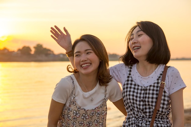 Amigos sorridente de pé contra o mar durante o pôr do sol