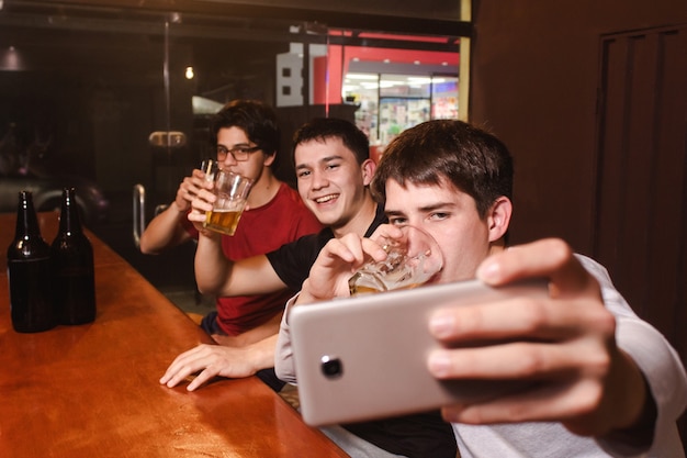 Amigos sorridentes felizes tomando uma selfie enquanto bebem cerveja no bar.