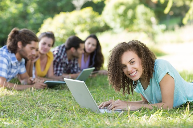 Amigos sorridentes no parque usando tablet pc e laptop