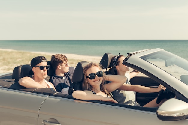 Amigos sorrindo, dirigindo o carro perto do mar e se divertindo