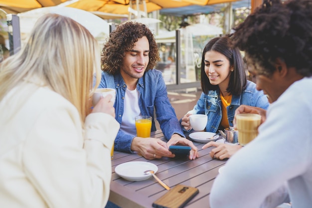 Amigos sorrindo usando telefone celular enquanto estão sentados na mesa