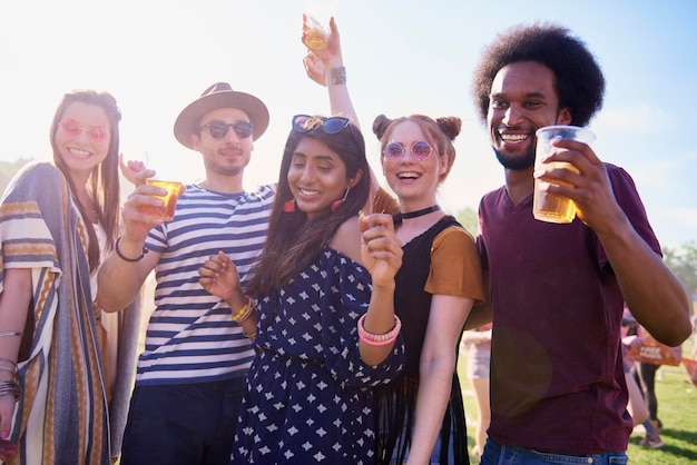 Amigos sosteniendo bebidas en vasos mientras bailan contra el cielo