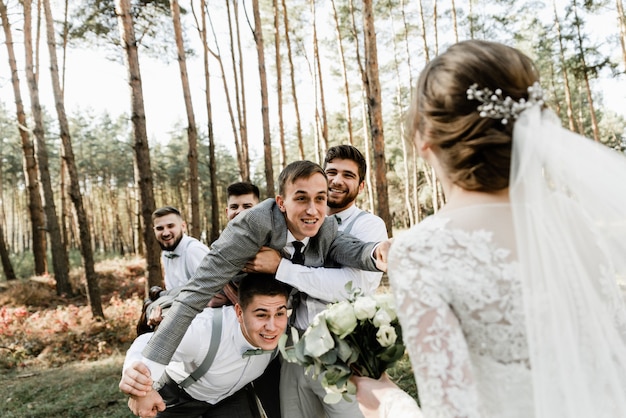 amigos sostienen en sus brazos a un novio divertido que se acerca a la novia para un beso