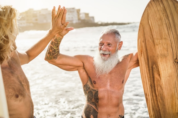 Amigos surfistas de várias gerações dão as mãos na praia após a sessão de surf - concentre-se no rosto do homem mais velho