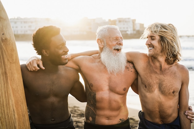 Amigos surfistas de várias gerações se divertindo na praia após a sessão de surf - Foco principal no rosto do homem certo