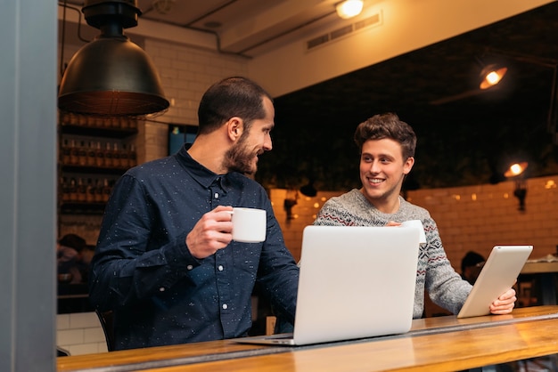 Amigos con tableta y computadora portátil en una cafetería.