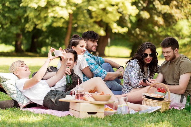 amigos con teléfonos inteligentes en un picnic en el parque de verano