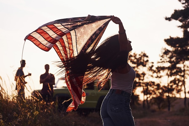 Foto amigos têm um bom fim de semana ao ar livre perto do carro verde deles com a bandeira dos eua