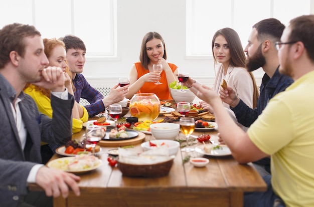 Amigos têm um jantar de festa no café, restaurante. Jovem empresa comemora com álcool e comida na mesa de madeira dentro de casa.