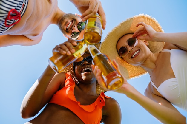 Foto amigos tintinean botellas con cerveza, vista inferior