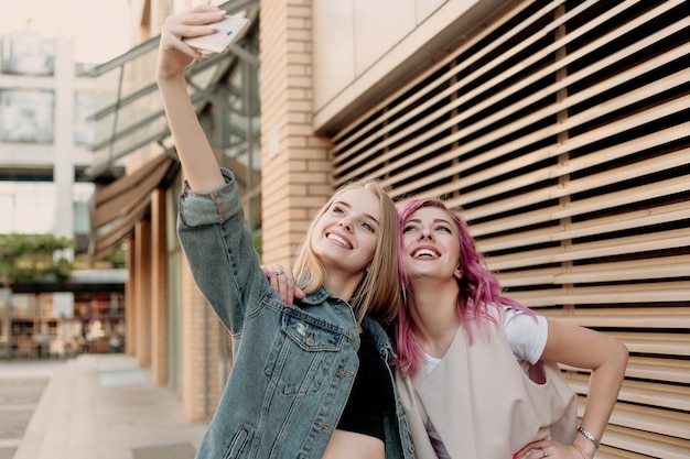 Amigos tirando selfie com um smartphone e fazendo caretas e se divertindo. Closeup de meninas fazendo caretas e sorrindo para selfie. Duas amigas felizes tirando foto com seu smartphone na cidade