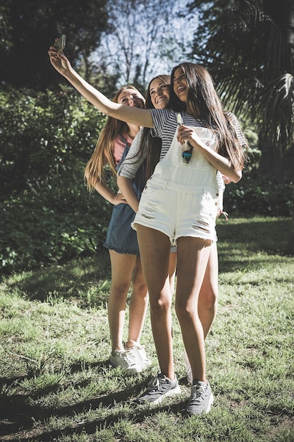 Foto amigos de toda la longitud tomando selfies mientras están de pie en el campo en el parque durante un día soleado