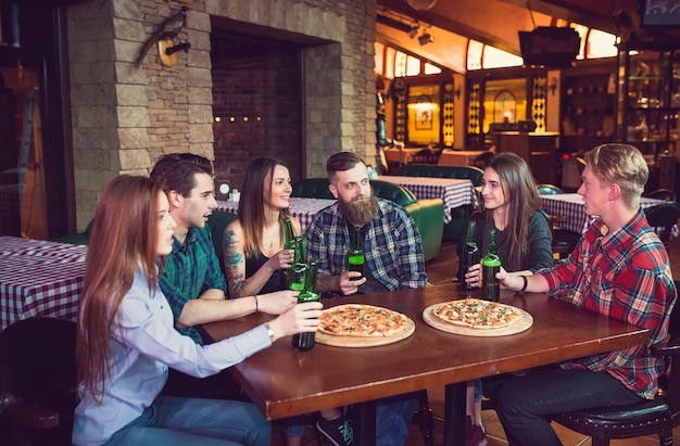 Amigos tomando bebidas y comiendo pizzas en un bar.