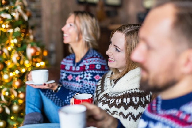 Amigos tomando café pasando el rato juntos cerca del árbol de navidad decorado