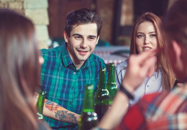 Amigos tomando una copa en un bar, están sentados en una mesa de madera con cervezas y pizza.