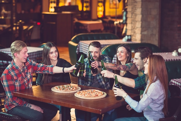 Amigos, tomar uma bebida em um bar, eles estão sentados em uma mesa de madeira com cervejas e pizza.