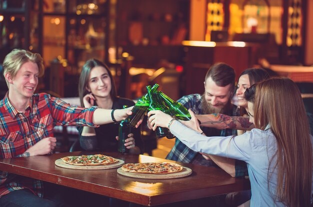 Amigos, tomar uma bebida em um bar, eles estão sentados em uma mesa de madeira com cervejas e pizza.