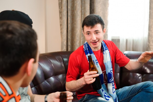 Amigos torcendo e bebendo álcool enquanto assistia jogo de futebol na tv.