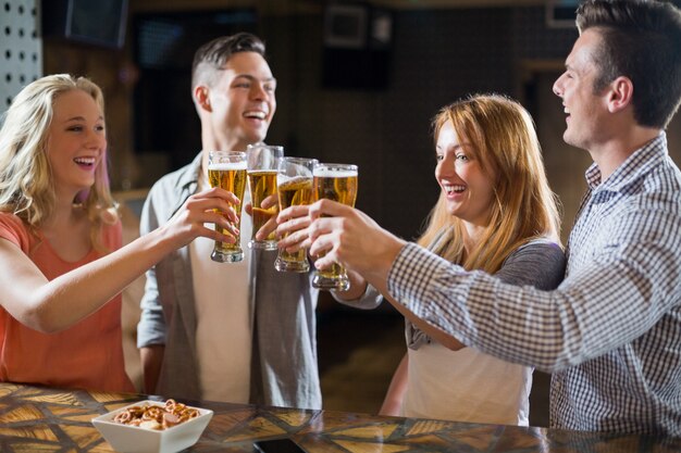 Amigos tostado vasos de cerveza en barra de bar