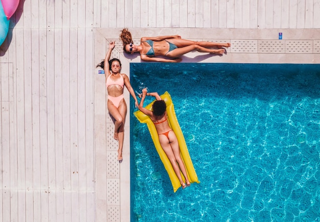 Amigos en traje de baño que se broncean en la tumbona de una piscina