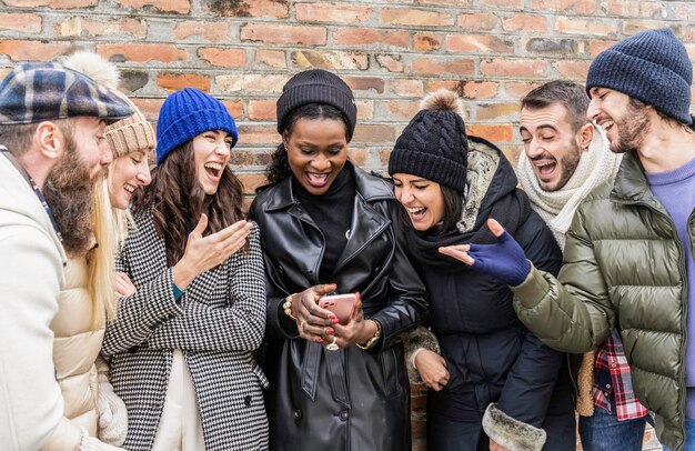 Amigos urbanos multiculturais se divertindo em dispositivos de telefonia móvel vestindo roupas quentes da moda Amigos multiculturais felizes compartilhando tempo juntos assistindo vídeos engraçados da moda no smartphone Filtro quente