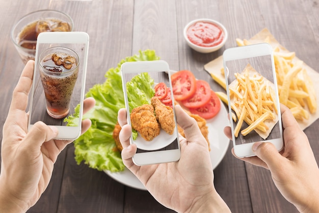 Amigos usando smartphones para tirar fotos de frango frito, batata frita e cola