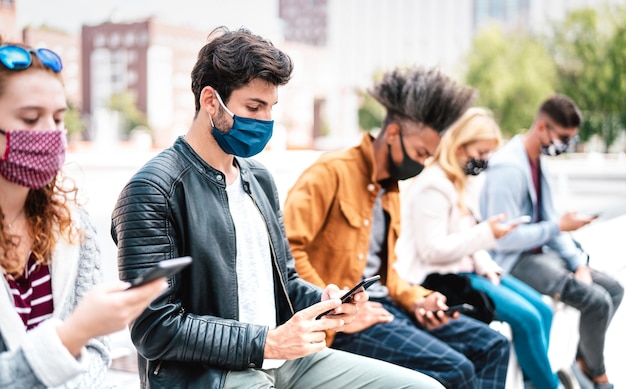 Amigos usando telefones celulares cobertos por máscara facial na segunda onda de covid - concentre-se no primeiro cara à esquerda