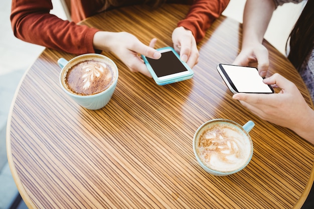 Amigos usando un teléfono inteligente y tomando un café en una cafetería