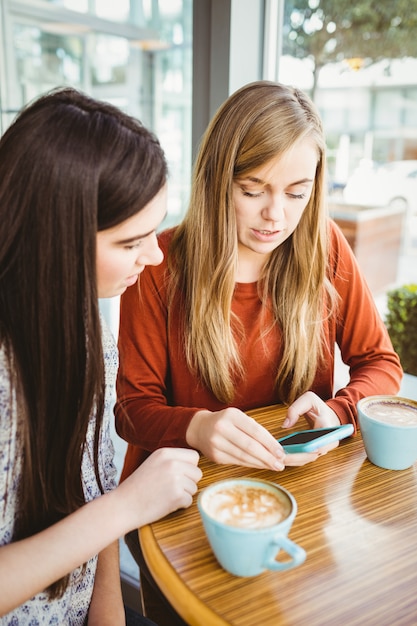 Amigos usando un teléfono inteligente y tomando un café en una cafetería