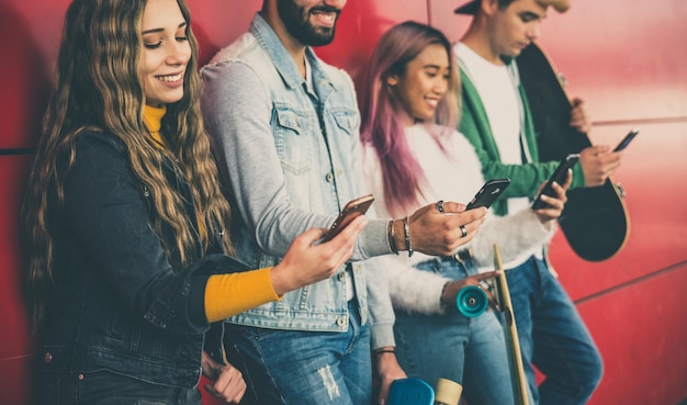 Foto amigos usando teléfonos inteligentes mientras están de pie contra la pared