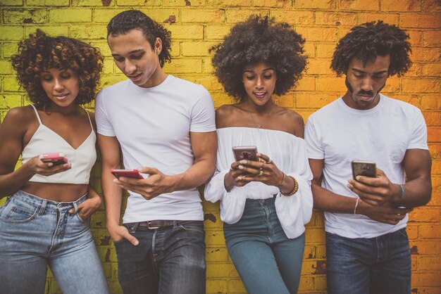 Foto amigos usando teléfonos mientras están de pie contra la pared