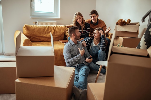 Amigos usando uma tecnologia enquanto relaxam durante a mudança para uma nova casa