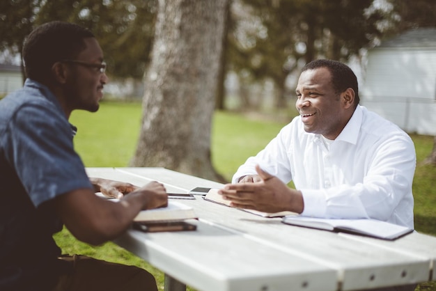 Amigos varones afroamericanos sentados en la mesa y leyendo la Biblia en la mesa