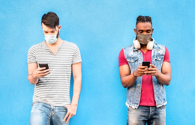 Amigos varones con máscaras faciales mediante la aplicación de seguimiento con teléfonos móviles inteligentes