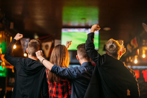 Amigos ve fútbol en la televisión en un bar deportivo