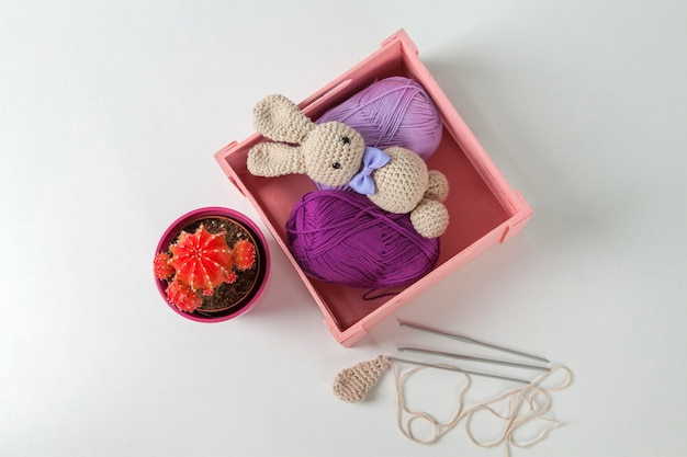 Amigurumi-Kaninchen mit schwarzen Augen und Fliege, Kaktus, Wollbox und Häkelnadeln