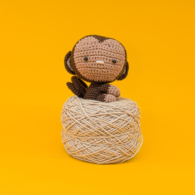 Amigurumi de mono sentado sobre un ovillo de lana color crema. fondo amarillo