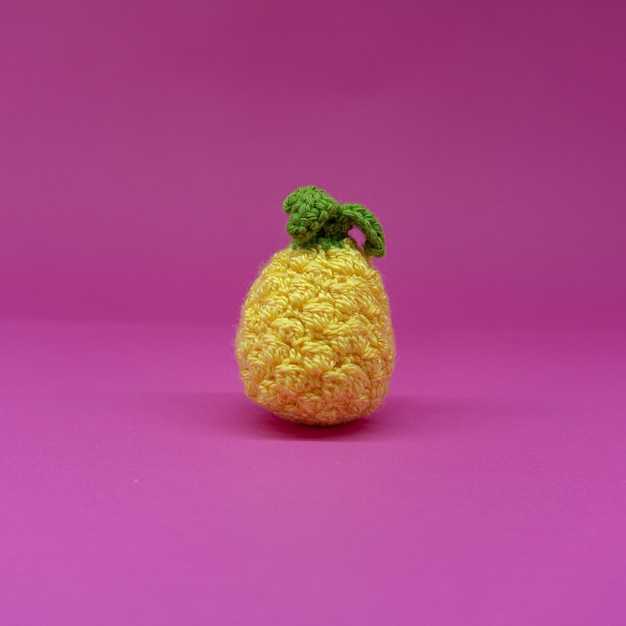 Amigurumi de piña, sobre fondo rosa.