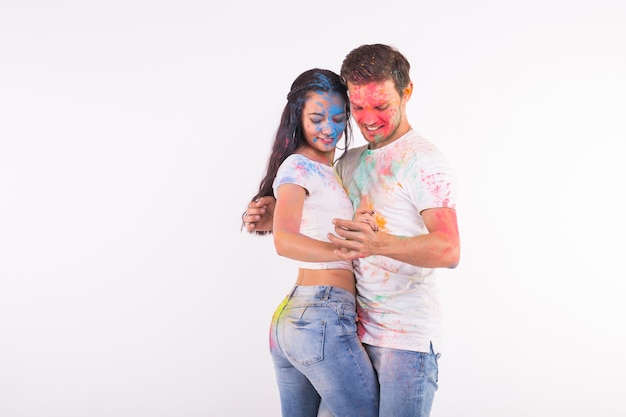 Amistad, baile social, amor, festival de holi, concepto de personas - pareja joven jugando con colores y bailando bachata o kizomba en el festival de holi en superficie blanca con espacio de copia