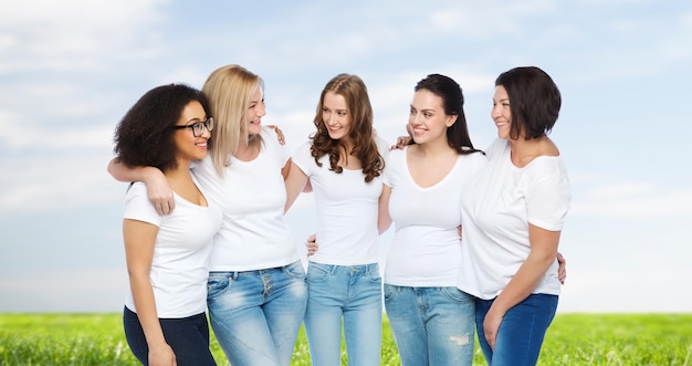 amistad, diversidad, cuerpo positivo y concepto de personas - grupo de mujeres felices de diferentes tamaños con camisetas blancas abrazándose sobre el cielo azul y el fondo de la hierba