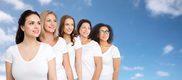 amistad, diversidad, cuerpo positivo y concepto de personas - grupo de mujeres felices de diferentes tamaños en camisetas blancas sobre cielo azul y fondo de nubes