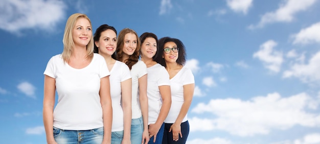 amistad, diversidad, cuerpo positivo y concepto de personas - grupo de mujeres felices de diferentes tamaños en camisetas blancas sobre cielo azul y fondo de nubes